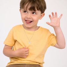 a young boy with his hand up in the air while wearing a yellow shirt and khaki pants