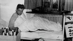 black and white photograph of a man laying on a bed with beer bottles in front of him