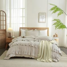 a bed with white linens and pillows in a bedroom next to a large green plant