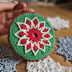 crocheted doily with red and white flowers on it being held by someone's hand