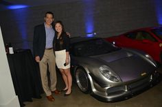 a man and woman standing next to a silver sports car