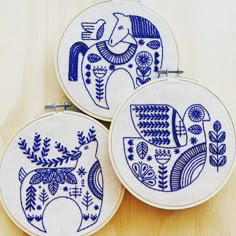 three blue and white embroidered hoop art pieces on a wooden surface with pins attached to the hoop