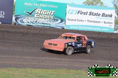 an orange truck driving on top of a dirt track in front of a green and white sign