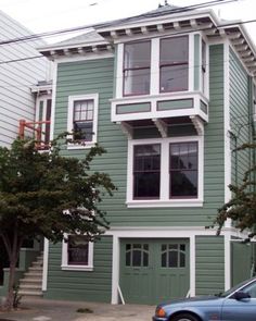 a car is parked in front of a green house with white trim and two story windows