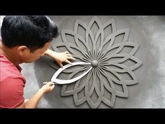 a man cutting paper with scissors in front of a circular design on a wall that has been carved into it