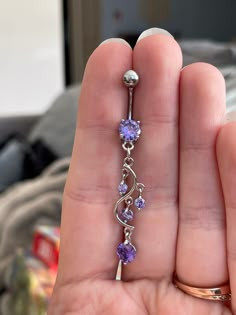 a person is holding a purple and white diamond navel ring in their left hand