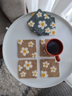 four coasters on a plate with a cup of coffee next to them and a small pot holder