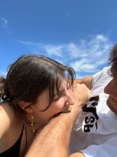 a man and woman sitting next to each other on the beach looking at something in the sky