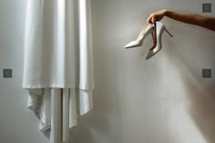 a woman's hand reaching for high heel shoes hanging on a wall next to a white dress