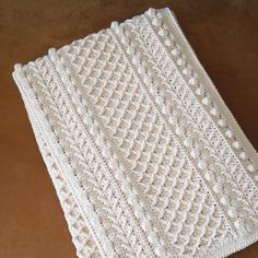 a white crocheted blanket sitting on top of a wooden table next to a cup