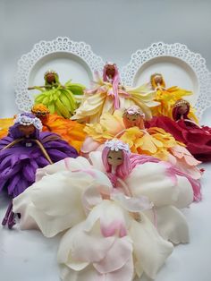 several small dolls sitting next to each other in front of white plates and flower decorations