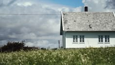 a small white house sitting on top of a lush green field next to a power line