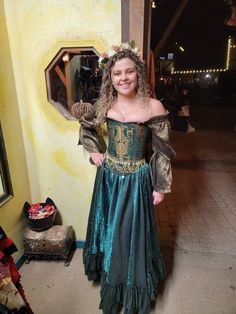 a woman in a green and gold dress standing next to a wall with a mirror