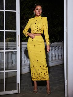 a woman standing in front of an open door wearing a yellow skirt and crop top