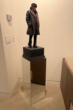 a statue of a man standing on top of a glass block in a room with white walls