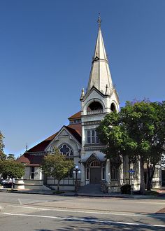 an old church sits on the corner of a street with trees in front of it