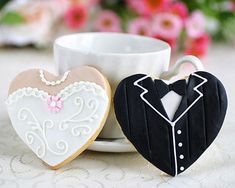 two cookies in the shape of heart and tuxedo are next to a coffee cup