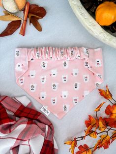 a pink bandana with white cats on it and fall leaves around it, including an orange pumpkin