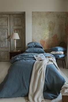 an unmade bed with blue sheets and pillows in a white room next to a wooden door