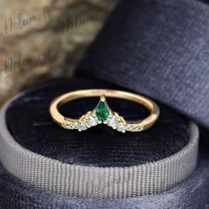 an emerald and diamond ring sitting on top of a velvet box