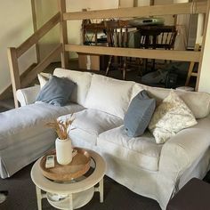 a living room with white couches and pillows on the top of each sofa, next to a coffee table