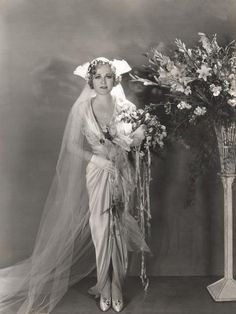 an old black and white photo of a woman in a wedding dress next to a vase with flowers