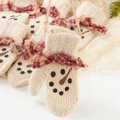 knitted snowman mittens hanging from strings on a white surface with pine branches