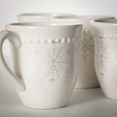 three white mugs with snowflakes on them sitting side by side in front of each other