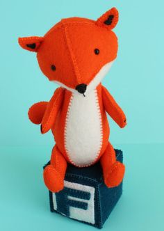 an orange stuffed animal sitting on top of a blue box with the letter f in it's mouth