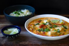 there is a bowl of soup next to two bowls of rice and limes on the table