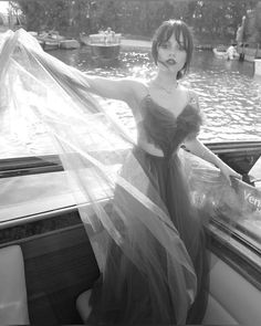 a woman in a long dress standing on the back of a boat with a veil over her head