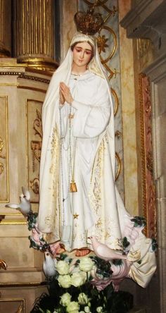 a statue of the virgin mary in front of a gold and white wall with flowers