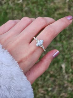 a woman's hand with a diamond ring on top of her finger and grass in the background