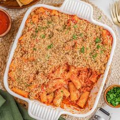 a casserole dish filled with pasta and sauce on a table next to silverware