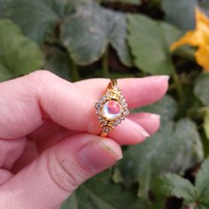 a woman's hand holding a gold ring with pink and white stones