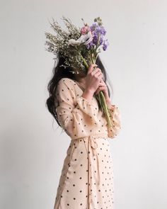 a woman in a polka dot dress holds flowers up to her face while standing against a white wall