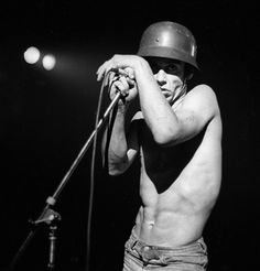 a shirtless man holding a microphone in his right hand and wearing a helmet on top of his head