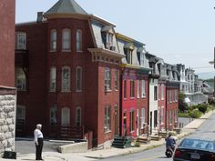 two men are standing on the sidewalk in front of row houses with red brick walls