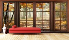 a red couch sitting in front of an open window with autumn leaves on the ground