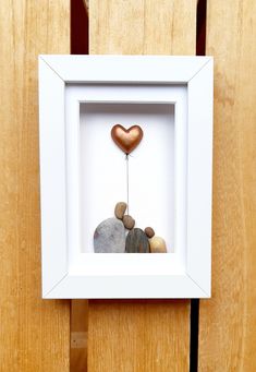 a white frame holding a heart shaped rock with a tiny tree in it on a wooden surface