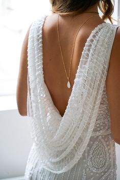 the back of a woman's white dress with pearls on it and a gold necklace