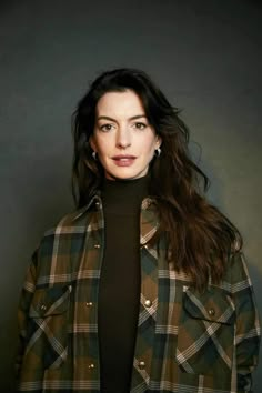 a woman with long dark hair wearing a green plaid jacket and black turtle neck sweater