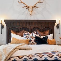 a bed with pillows and blankets on it in front of a wall mounted deer head