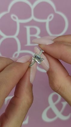 two hands with pink manicures holding an engagement ring and diamond on their fingers