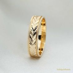 a gold wedding ring with an arrow pattern on it's side, sitting on a white background