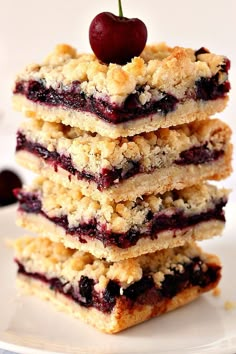 a stack of blueberry crumb bars sitting on top of a white plate next to a cherry