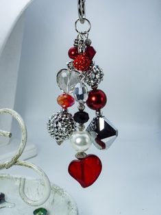 a red heart hanging from a chain with charms attached to it's sides, on a white surface