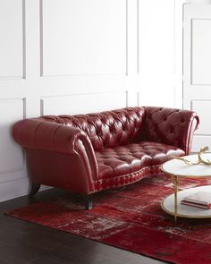 a red leather couch sitting on top of a wooden floor next to a white table