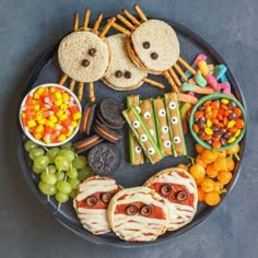 a black plate topped with sandwiches and crackers covered in halloween food next to candy