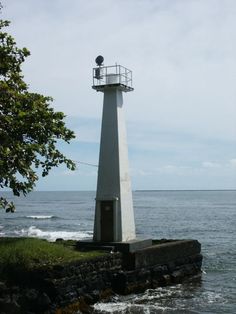 a white light house sitting on top of a rock wall next to the ocean with waves coming in